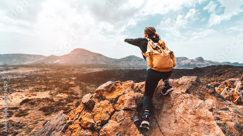 Beautiful hiker woman on the top of the mountain pointing at the sunset valley. Girl with backpack travel alone in the nature.