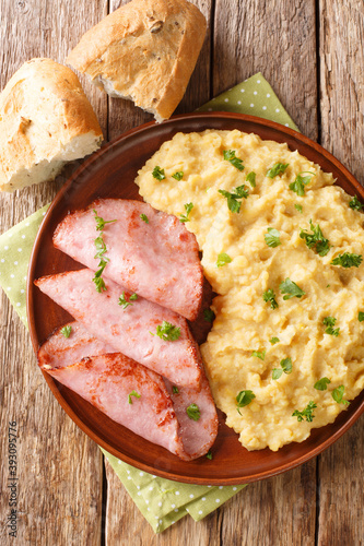 pease pudding is made from cooking yellow split peas served with fried ham closeup in the plate on the table. Vertical top view from above