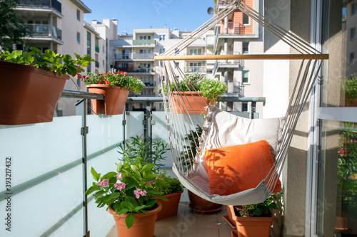 a sunny balony with flowers and potted plants and hammock with orange pillow
