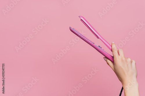 partial view of woman holding hair straightener in hand isolated on pink