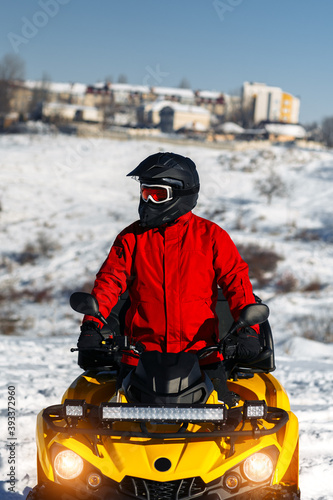 Close-up image of young man driver on the ATV quad bike stand in heavy snow with deep wheel track. Moto winter sports.