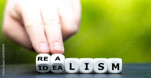 Hand turns dice and changes the word "idealism" to "realism".