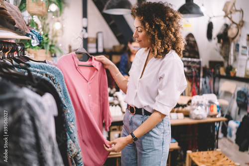 Caucaisan female customer with curly hair buying clothes in boutique using fitting concept while choosing, professional stylist creating trendy look concentrated on selection in designer shop