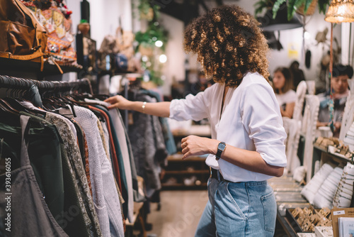 Caucaisan female customer with curly hair buying clothes in boutique using fitting concept while choosing, professional stylist creating trendy look concentrated on selection in designer shop