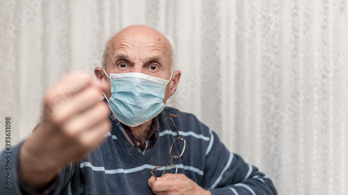 angry aggressive elderly man wearing face mask showing big fist self isolation and coronavirus concept