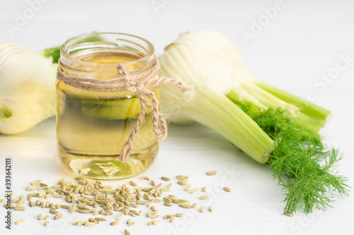 Glass bottle of fennel essential oil with fennel seeds and bulb on wooden table. Herbs alternative medicine background concept