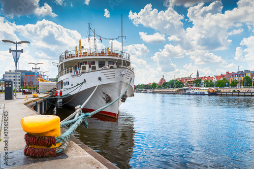 Large boat docked or moored on Customs Quay, view on promenade and boulevards on Odra River embarkment with old town in background in Szczecin, Poland