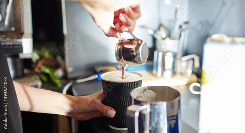 Barista pours espresso coffee in to disposable paper cup. Making tasty coffee drink with milk. Blurred image, selective focus