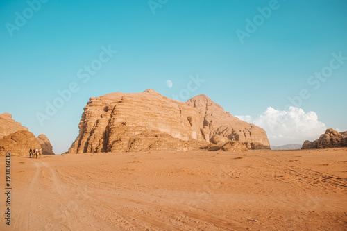 People on camels pass the sand dunes in the desert, which is surrounded by stone rocks and pink sand, animals walk without getting tired,there is not enough water, and the hot hot sun burns everything
