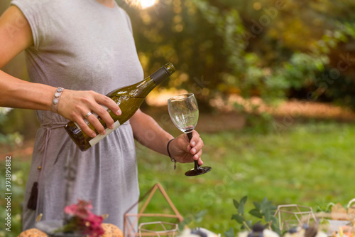 Anonymous woman pouring a glass of white wine at a relaxed garden party.