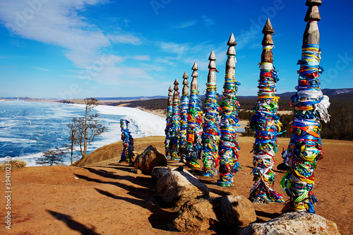 Wooden ritual pillars with colorful ribbons on cape Burhan or Shamanka rock. Lake Baikal, Olkhon Island in winter.
