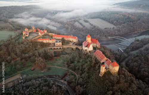 Aerial view of the large and beautiful Moravian royal castle Veveri (Burg Eichhorn), standing on a rock above water dam on the river Svratka, early morning light and autumn weather with the green fore