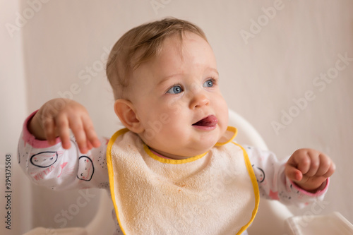 One-year-old girl with her tongue out and a bib in a high chair.