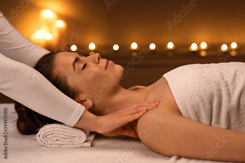 Unrecognizable masseuse massaging relaxed lady shoulders, spa interior