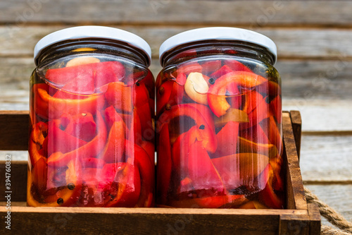 Wooden crate with glass jars with pickled red bell peppers.Preserved food concept, canned vegetables isolated in a rustic composition.