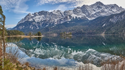 Reflecting mountain lake with small islands in front of snowy mountains in the german alps. Panorama of a reflecting mountain lake.