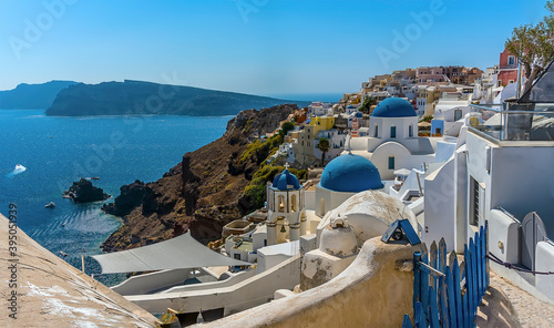 A panorama view of white painted houses, pathways and blue domed churches in the village of Oia, Santorini in summertime