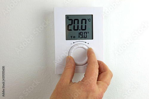 hand with thermometer controlling a homes heating.