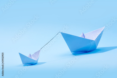 Paper boats - Tugboat or Remorker pulling a big boat on blue background. Little helper concept, Tugboat