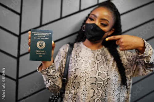 African woman wearing black face mask show Liberia passport in hand. Coronavirus in Africa country, border closure and quarantine, virus outbreak concept.