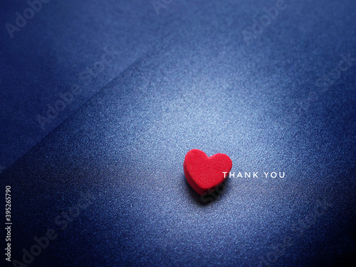 The word Thank You and red heart on glittering dark blue paper background.