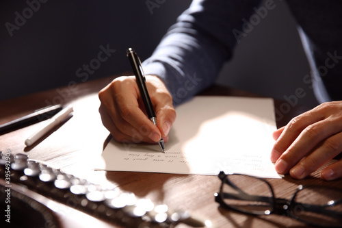 Man writing letter at wooden table indoors, closeup