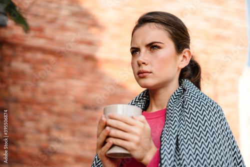 Charming serious girl drinking coffee while sitting in cafe outdoors