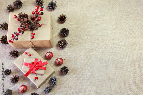 Ekologiczne tło bożonarodzeniowe w neutralnych kolorach z prezentami, szyszkami, czerwonymi ozdobami i tkaniną z juty