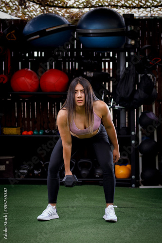 mujer con cuerpo atlético haciendo ejercicios en gimnasio al aire libre, usando ropa deportiva y mancuernas. Entrenadora personal con cuerpo 