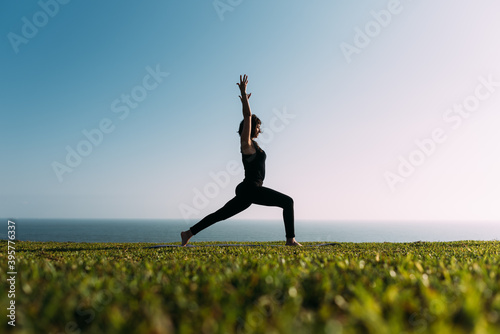 Mujer adulta delgada estira sus brazos al cielo practicando yoga en la tarde en exteriores.
