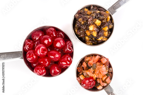 Close up silver measuring cups containing maraschino cherries, mincemeat, and fruit cake mix top down view