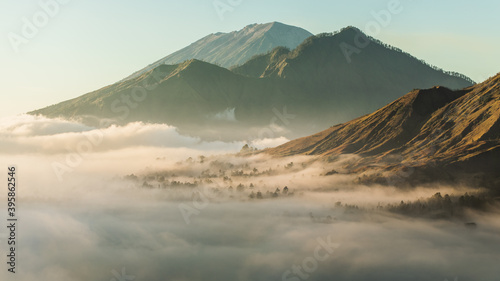 Sunrise view of mount Batur, Abang and Agung volcano in Bali from Pinggan village. Beautiful sunrise and low clouds. Layered minimalist landscape.