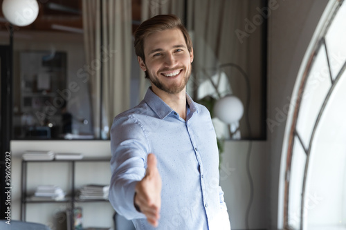 Portrait of happy young male hr stretching hand inviting you spectator to join corporate team, friendly capable manager looking at camera extending hand for handshake welcoming new client or colleague