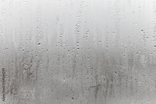 Natural drops of water flow down the glass, high humidity in the room, condensation on the glass window. Neutral colors. Excellent background with condensation drops texture
