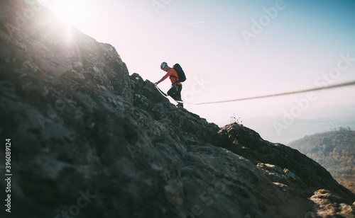 Mountaineer with backpack using climbing rope to climb rocky mountain summit