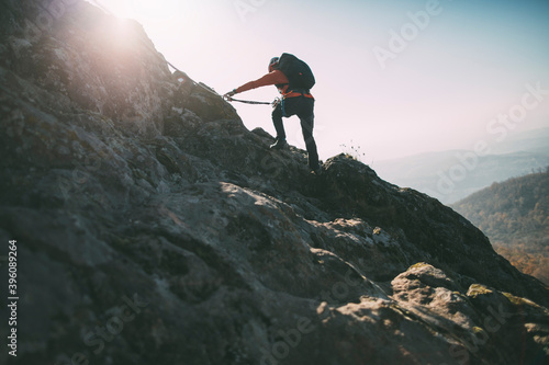 Mountaineer climbing rocky summit. Rear view of climber reaching top along via ferrata