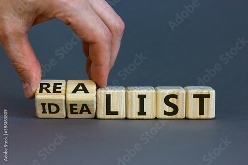 Idealist or realist. Male hand flips wooden cubes and changes the word 'idealist' to 'realist' or vice versa. Beautiful grey background, copy space. Idealist or realist concept.