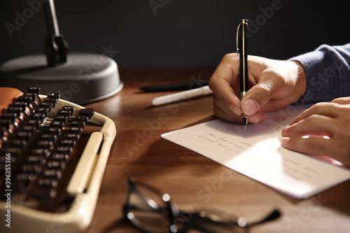 Man writing letter at wooden table indoors, closeup