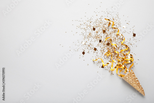 Golden confetti and streamers with party cracker on white background, top view. Space for text