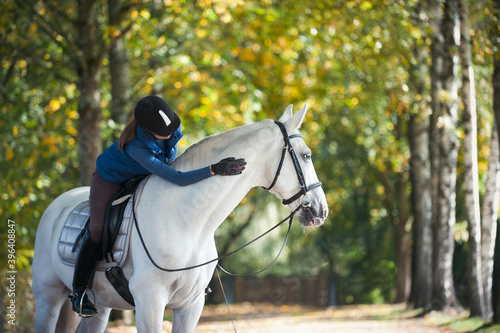 Equestrian lady riding horseback stroking white horse neck