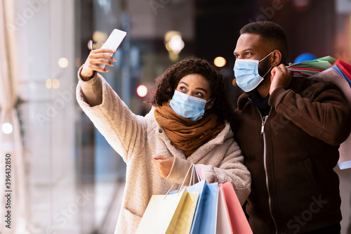 Black couple in masks taking selfie after shopping