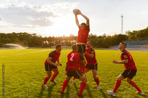 Full length image of a group of men in sports equipment play rugby on a sports field outside.