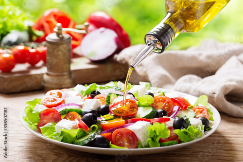 olive oil pouring into plate of fresh greek salad