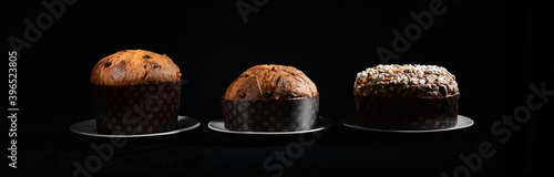 three types of Italian panettone: high, low and with almonds on a black background on a dish with cutting light