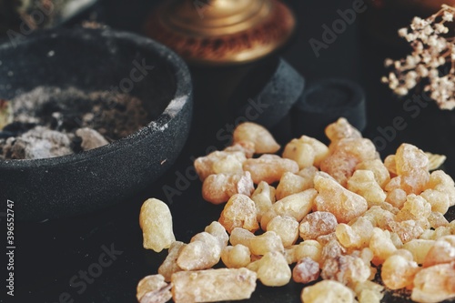 Many small peaces of yellow Yemen frankincense from boswellia tree. Dark black background with charcoal and iron cast ashtray. Closeup with blurry background. Dark, mysterious elegant classy chic mood