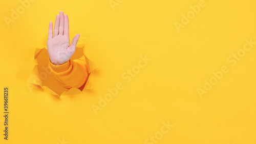 Woman hand arm showing stop gesture with palm isolated through torn yellow wall background studio. Copy space advertisement place for text mage promotional content. Advertising area workspace mock up.