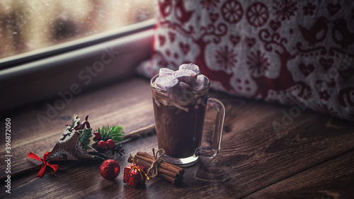 Hot chocolate christmas drink with marshmallows and cinnamon sticks christmas red box gift and decorations by the window cozy relaxing winter atmosphere snowing