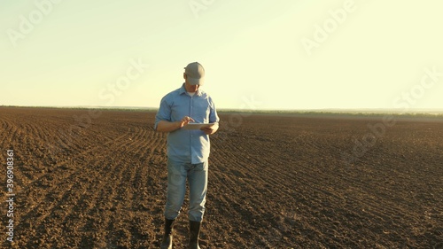 A farmer works with a tablet in a plowed field in sun. agronomist with a tablet studying the harvest of sowing grain in the field. a business person plans his income in this area. grain harvest.