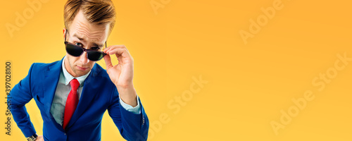 Are you seriously?! Funny skeptic businessman in blue confident suit and red tie, looking through sunglasses, copy space empty area for some text or slogan, over yellow-orange color background.