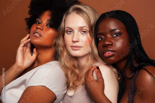 young pretty caucasian, afro, scandinavian woman posing cheerful together on brown background, lifestyle diverse nationality people concept